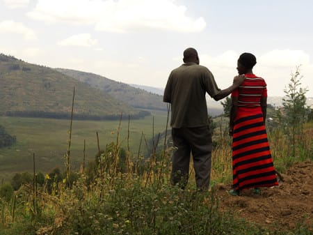 A black couple look over green rural landscape, the man's hand is on the women's shoulder