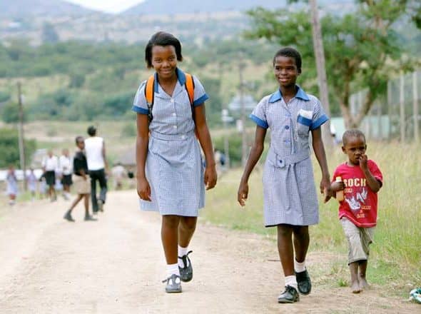 Two black schoolgirls and a young black boy walking in a street in South Africa