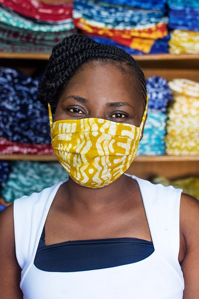 Photo of young black woman in fabric workshop wearing facemask looking at camera