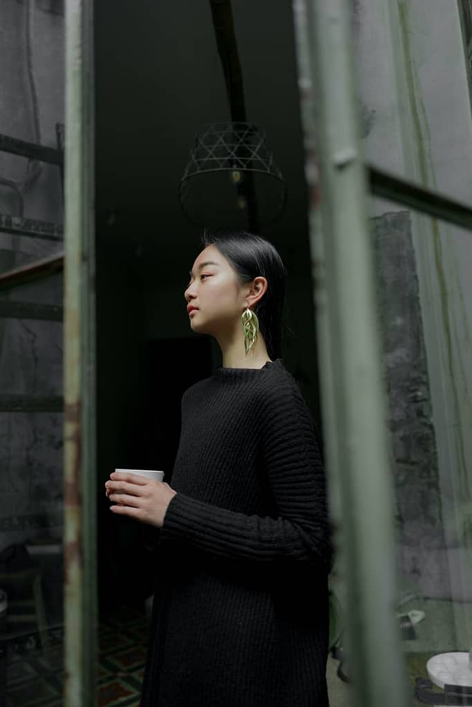 Southeast Asian young woman standing in a doorway holding a drink and looking into the distance
