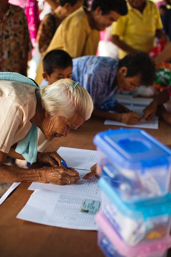 Older Woman Signing Papers To Receive Health Package In Thailand