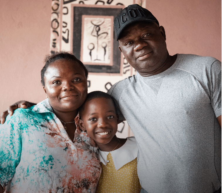 A black family of three, a women, man and girl smiling with their arms around each other.