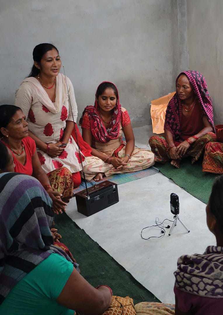 Group Of South Asian Women Sitting Around A Radio Transmitter And Recording Device