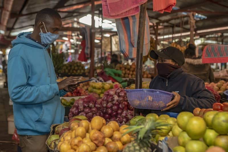 Photo of African man and woman wearing facemasks buying and selling fruits at market