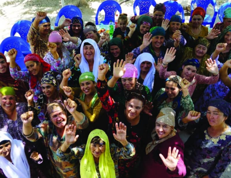 Photo of large group of Middle Eastern women wearing head coverings with raised hands smiling at camera