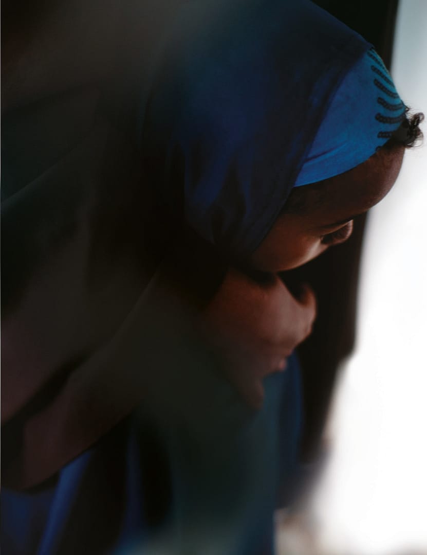Close Up Of Black Child Wearing Headscarf With An Adult's Hand On Their Shoulder