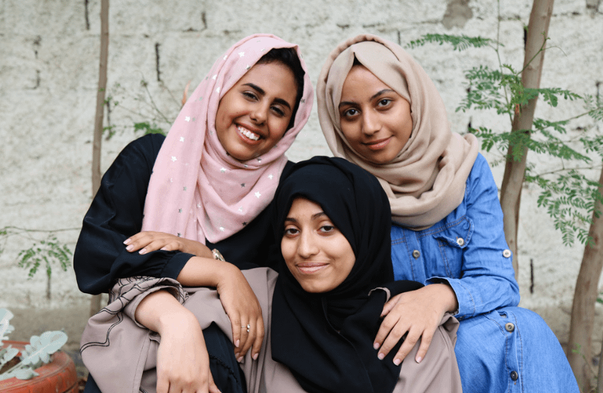 Three Teenage Girls Wearing Headscarves Smiling And Hugging