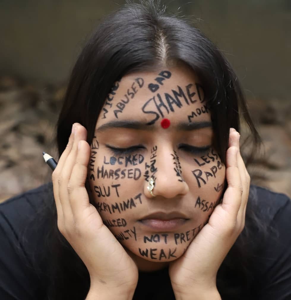 Photo of young southeast Asian woman with her head in her hands with abusive words written across her face, for examples bad and shamed