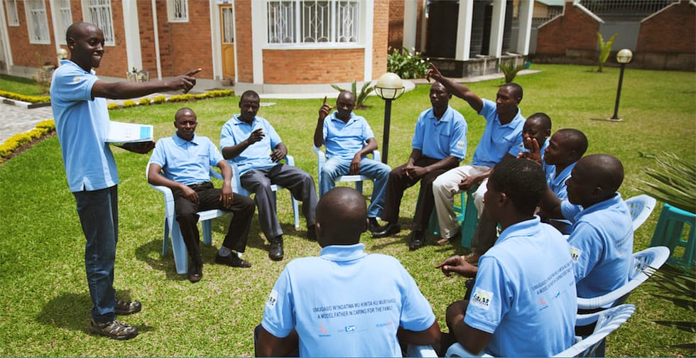 Photo of Rwandan men in workshop sitting in a circle, the facilitator is stood up