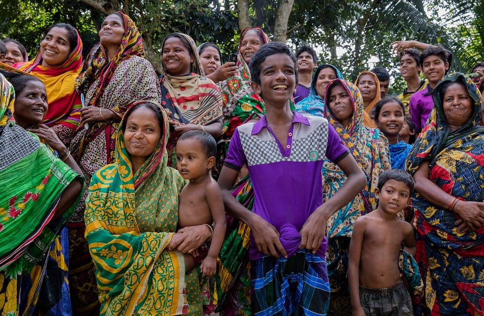 Group of smiling Bangladeshi women and children in colourful clothing.
