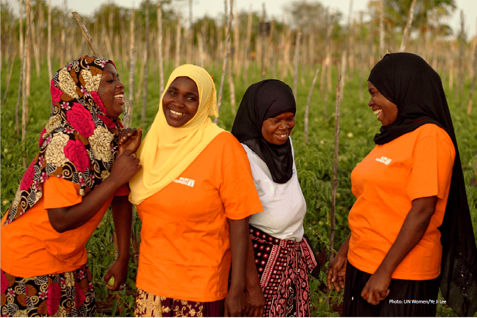 Group of black women wearing headscarves and UN Women t-shirts standing and laughing in a field