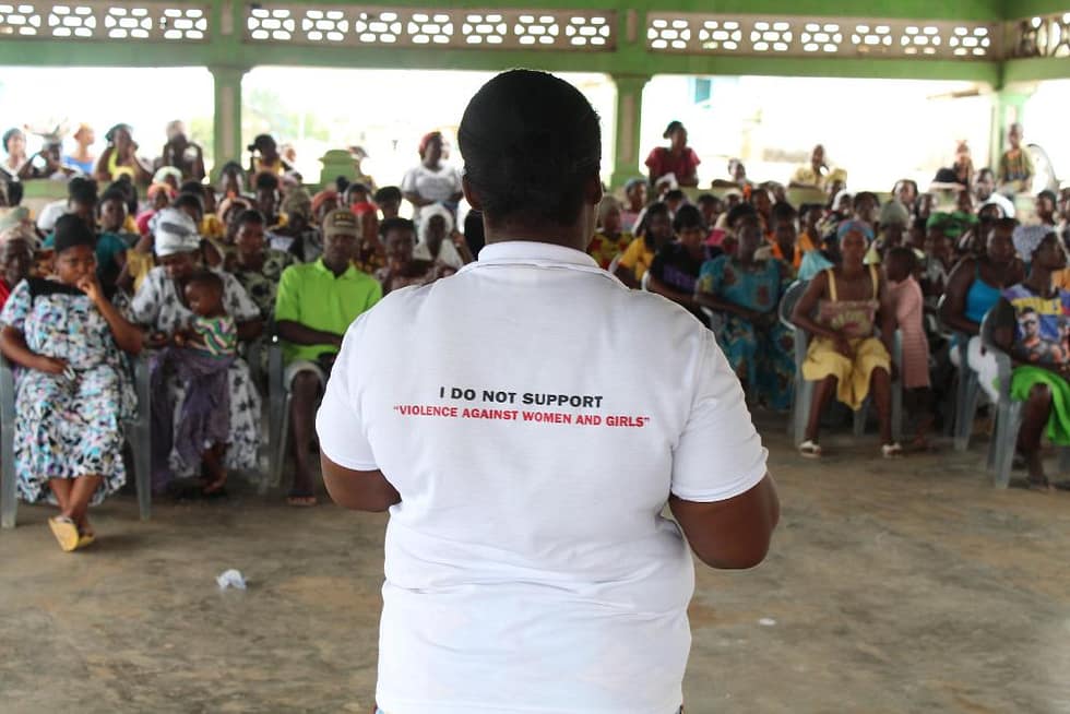 Facilitator in front of a crowd wearing a t-shirt that says I do not support violence against women and girls