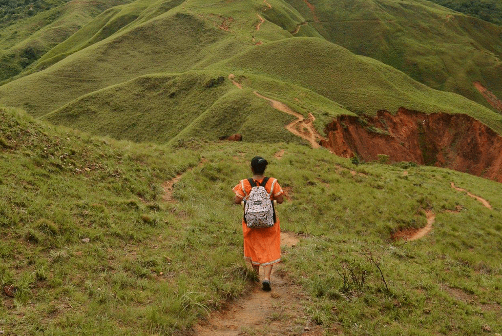 A woman is walking through a greenery hill with a backpack.