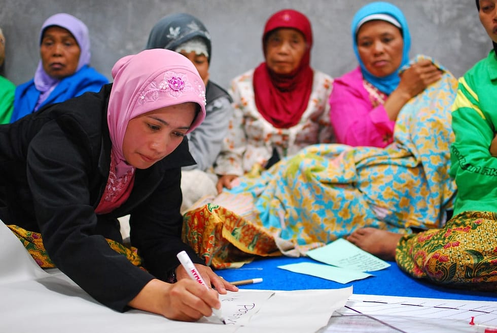 Photo of women of colour in headscarves sitting, one woman is writing on a large piece of paper