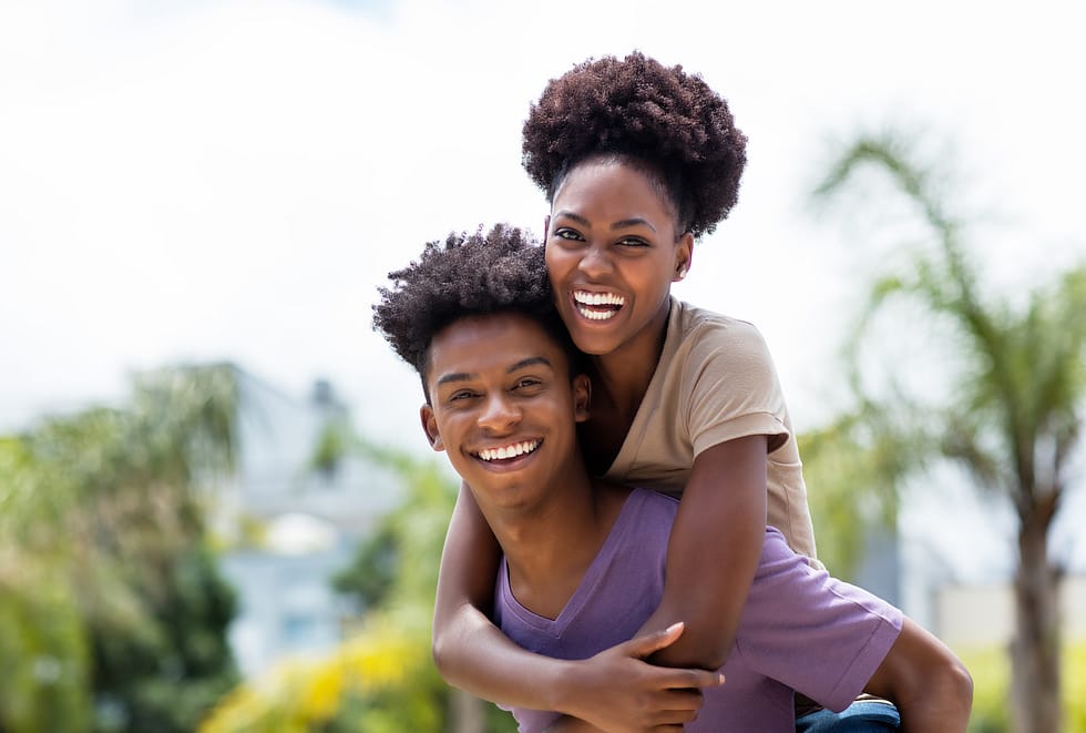 Black couple smiling and laughing, the young man is carrying the young women on his back