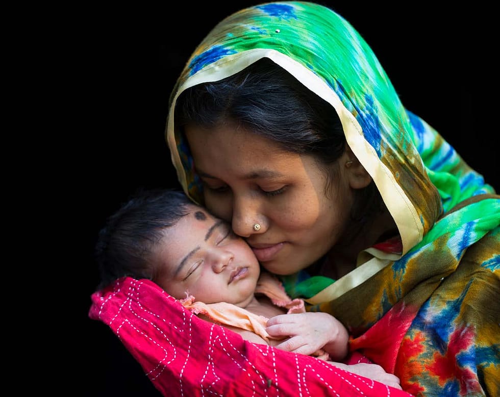 South Asian woman wearing a headscarf holding her baby and smiling